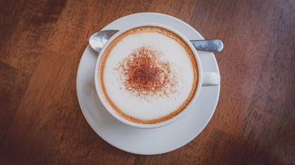 Hot coffee, white cups, plate, spoon and tissue all on the brown wooden table.