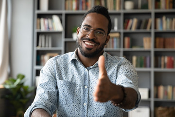 Headshot portrait of smiling african American young male employer stretch hand welcoming newcomer...