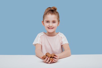 portret of little girl with walnuts in hand isolated on blue background, sitting at a table