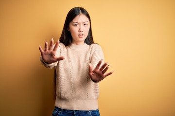 Young beautiful asian woman wearing casual sweater over yellow isolated background doing stop gesture with hands palms, angry and frustration expression