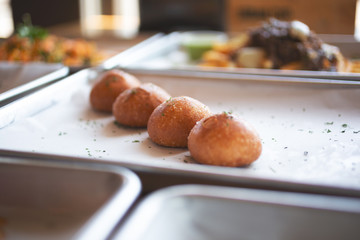 A view of four pieces of golden char siu bao Chinese dumplings among several other street food dishes in a restaurant or kitchen setting.