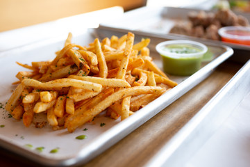 A closeup view of an appetizer tray of cajun style french fries, in a restaurant or kitchen setting.