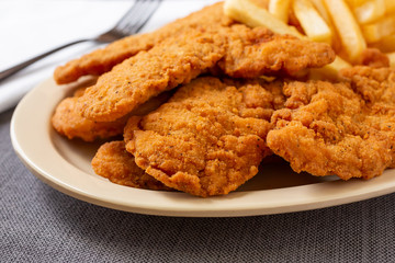 A closeup view of a plate of chicken tenders and french fries, in a restaurant or kitchen setting.