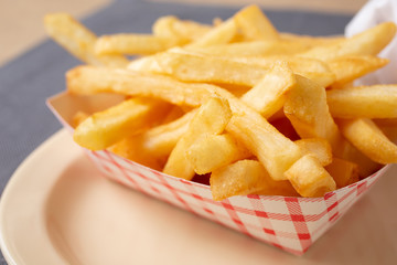 A closeup view of a carton of french fries, in a restaurant or kitchen setting.