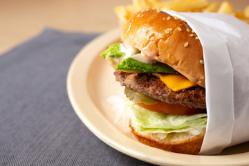 A closeup side view of a wrapped cheeseburger, in a restaurant or kitchen setting.