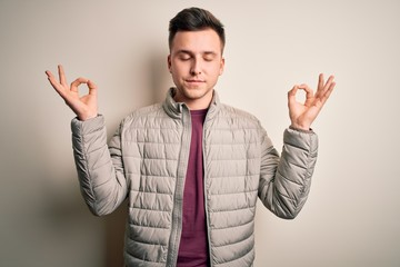 Naklejka premium Young handsome caucasian man wearing casual winter jacket standing over isolated background relax and smiling with eyes closed doing meditation gesture with fingers. Yoga concept.