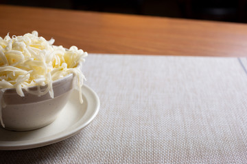 A view of a small bowl of shredded mozzarella cheese, cut off on the left side of the frame, in a restaurant or kitchen setting.