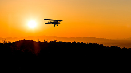 Fototapeta na wymiar Composite of a bi-plane flying over a desert landscape silhouetted by the setting sun