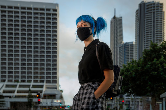 young female wearing medical mask in modern city street, stylish trendy girl with blue hair wearing fashionable protective medical mask amid coronavirus fears, covid19 pandemic, new fashion concept