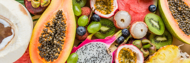 Fresh exotic fruits and tropical palm leaves on pastel orange background - papaya, mango, pineapple, passion fruit, dragon fruit, grapes, lichee, kiwi, melon. Healthy food and diet concept