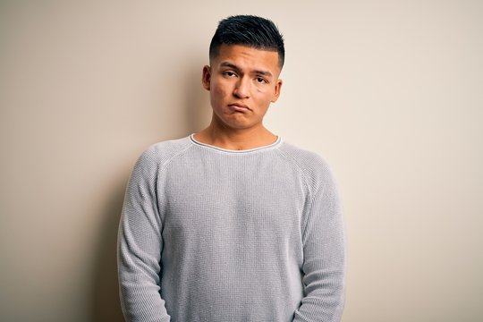 Young handsome latin man wearing casual sweater standing over isolated white background depressed and worry for distress, crying angry and afraid. Sad expression.