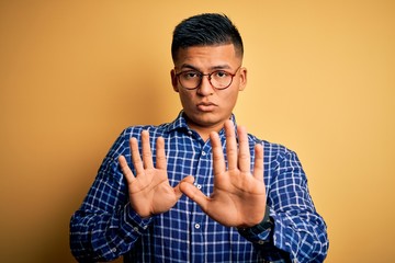 Young handsome latin man wearing casual shirt and glasses over yellow background Moving away hands...