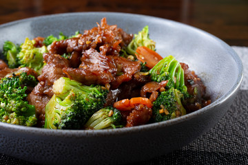 A side view of a bowl of beef broccoli, in a restaurant or kitchen setting.