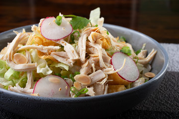 A closeup view of a bowl of Asian chicken salad, in a restaurant or kitchen setting.