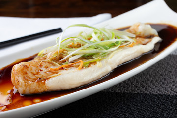 A closeup view of a plate of poached cod, in a restaurant or kitchen setting.