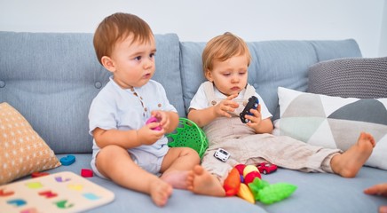 Beautiful toddlers sitting on the sofa playing with toys at home