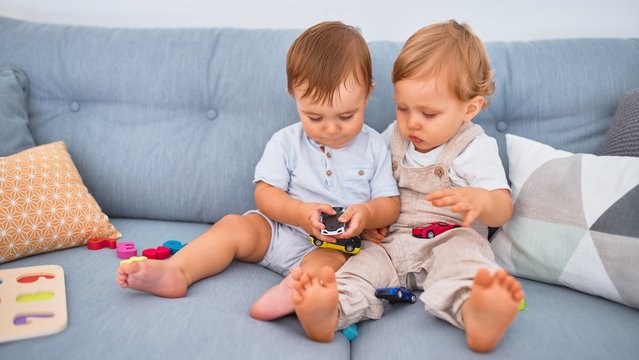 Beautiful toddlers sitting on the sofa playing with toys at home