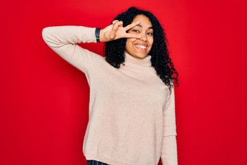 Young african american curly woman wearing casual turtleneck sweater over red background Doing...