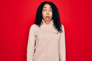 Young african american curly woman wearing casual turtleneck sweater over red background afraid and shocked with surprise and amazed expression, fear and excited face.