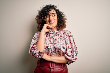 Young beautiful curly arab woman wearing floral t-shirt standing over isolated white background with hand on chin thinking about question, pensive expression. Smiling with thoughtful face. Doubt