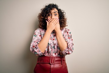 Young beautiful curly arab woman wearing floral t-shirt standing over isolated white background shocked covering mouth with hands for mistake. Secret concept.