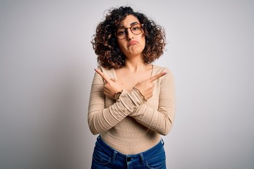 Young beautiful curly arab woman wearing casual t-shirt and glasses over white background Pointing to both sides with fingers, different direction disagree