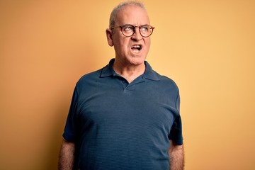 Middle age handsome hoary man wearing casual polo and glasses over yellow background angry and mad screaming frustrated and furious, shouting with anger. Rage and aggressive concept.