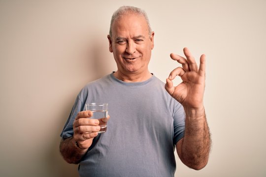 Middle age handsome hoary man drinking glass of water over isolated white background doing ok sign with fingers, excellent symbol