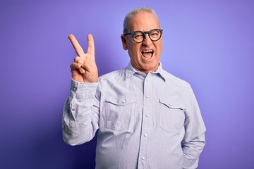 Middle age handsome hoary man wearing striped shirt and glasses over purple background smiling with happy face winking at the camera doing victory sign. Number two.