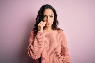 Young beautiful woman with curly hair wearing casual sweater over isolated pink background mouth and lips shut as zip with fingers. Secret and silent, taboo talking