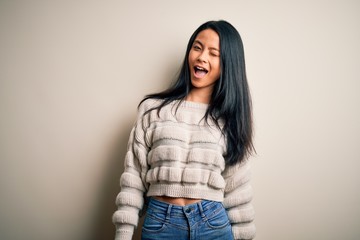 Young beautiful chinese woman wearing casual sweater over isolated white background winking looking at the camera with sexy expression, cheerful and happy face.