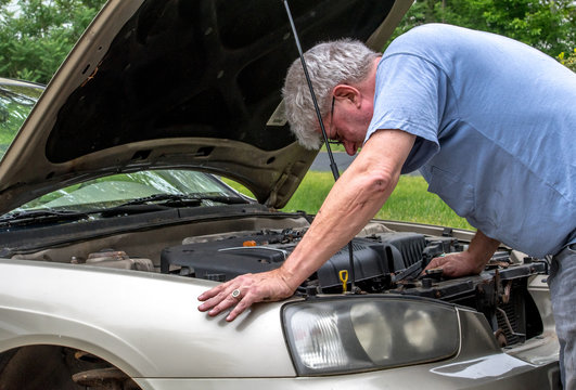 A senior male works under the hood of his car as he does auto repair in his driveway to save money