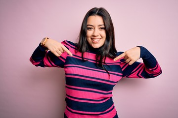 Young brunette elegant woman wearing striped shirt over pink isolated background looking confident with smile on face, pointing oneself with fingers proud and happy.