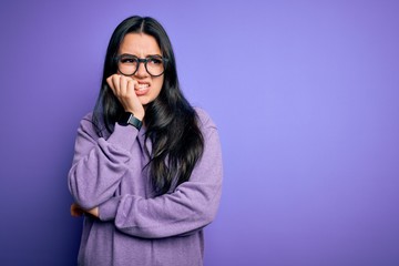 Young brunette woman wearing glasses over purple isolated background looking stressed and nervous with hands on mouth biting nails. Anxiety problem.