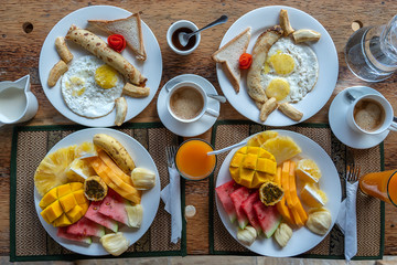 Tropical breakfast of fruit, coffee and scrambled eggs and banana pancake for two on the beach near sea