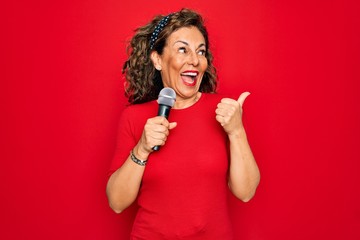Middle age senior singer woman singing using music microphone over red background pointing and...