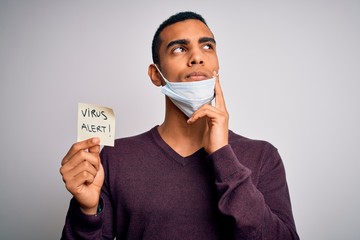 Young handsome african american man wearing medical mask holding virus alert reminder serious face thinking about question, very confused idea