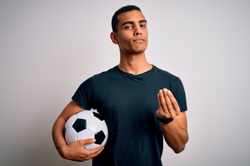 Handsome african american man playing footbal holding soccer ball over white background doing money...