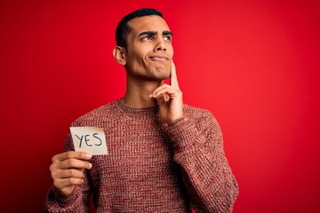 Young handsome african american man holding reminder paper with yes message serious face thinking...