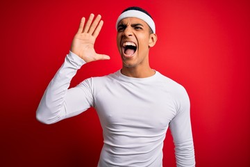Fototapeta premium Young handsome african american sportsman wearing sportswear over red background shouting and screaming loud to side with hand on mouth. Communication concept.