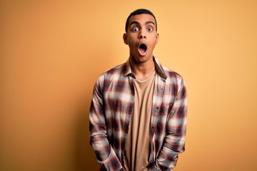 Fototapeta premium Young handsome african american man wearing casual shirt standing over yellow background afraid and shocked with surprise and amazed expression, fear and excited face.