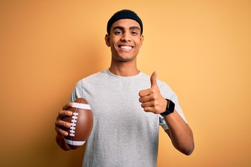 Young handsome african american man holding rugby ball over isolated yellow background happy with...