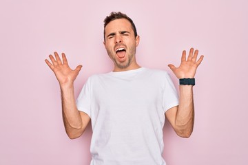 Handsome man with blue eyes wearing casual white t-shirt standing over pink background celebrating...