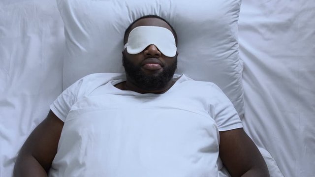 Exhausted man in sleep mask trying to fall asleep after long flight, jet lag