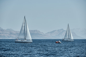 Obraz premium The rubber boat of organizers of a regatta with the judge and balloon of orange color, The race of sailboats, Intense competition, island with windmills are on background