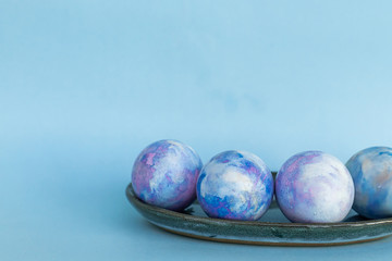 Colorful space-colored Easter egg in the plate on a blue background. Happy Easter card with copy space for text. Minimal style.