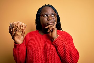 Young african american plus size woman with braids holding bowl with healthy peanuts serious face...