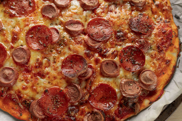 Macro photography of a homemade pepperoni and sausage pizza on metal tray with a black napkin in a wooden table. Details of food