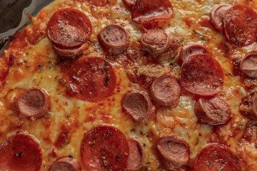 Macro photography of a homemade pepperoni and sausage pizza on metal tray with a black napkin in a wooden table. Details of food