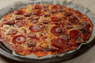 Overhead photography of a homemade pepperoni and sausage pizza on metal tray with a black napkin in a wooden table